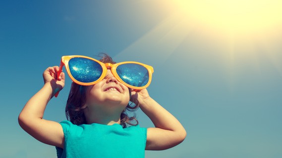 Kid with sunglasses on looking up to the sun